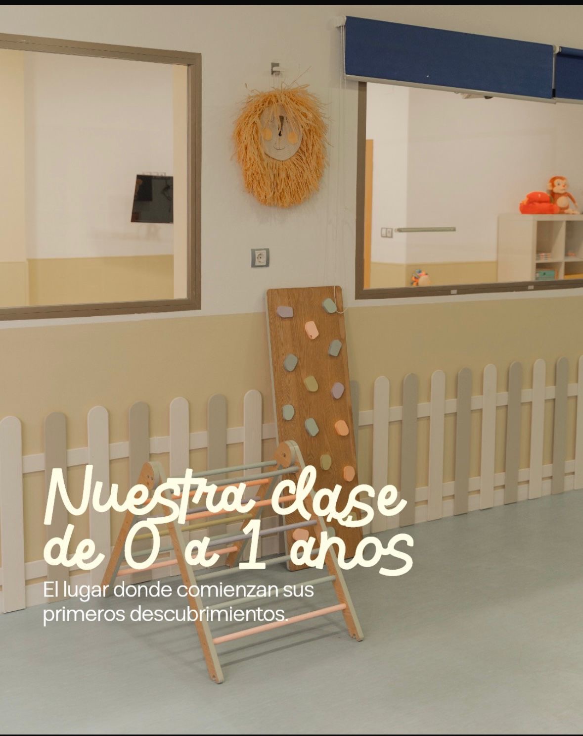 Aula de bebés con un triángulo de escalada de madera y una rampa con agarres, junto a una valla baja. Texto en la imagen: nuestra clase de 0 a 1 años, el lugar donde comienzan sus primeros descubrimientos.