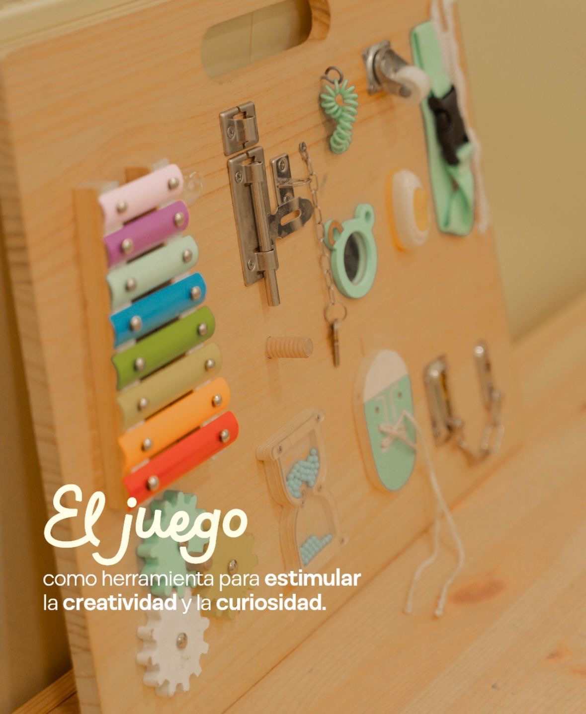 Panel de actividades de madera con xilófono, pestillos, cierres y engranajes para manipular. Texto en la imagen: el juego como herramienta para estimular la creatividad y la curiosidad.