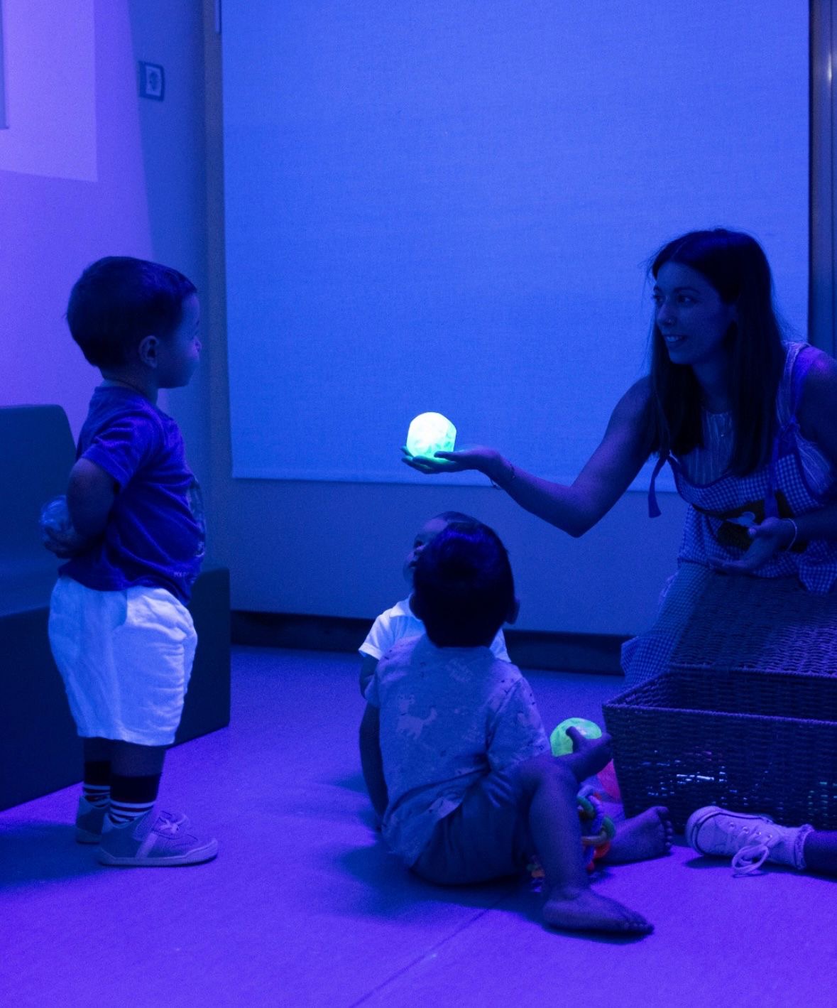 Una tutora muestra una lámpara luminosa a dos niños sentados en el suelo de la sala sensorial.